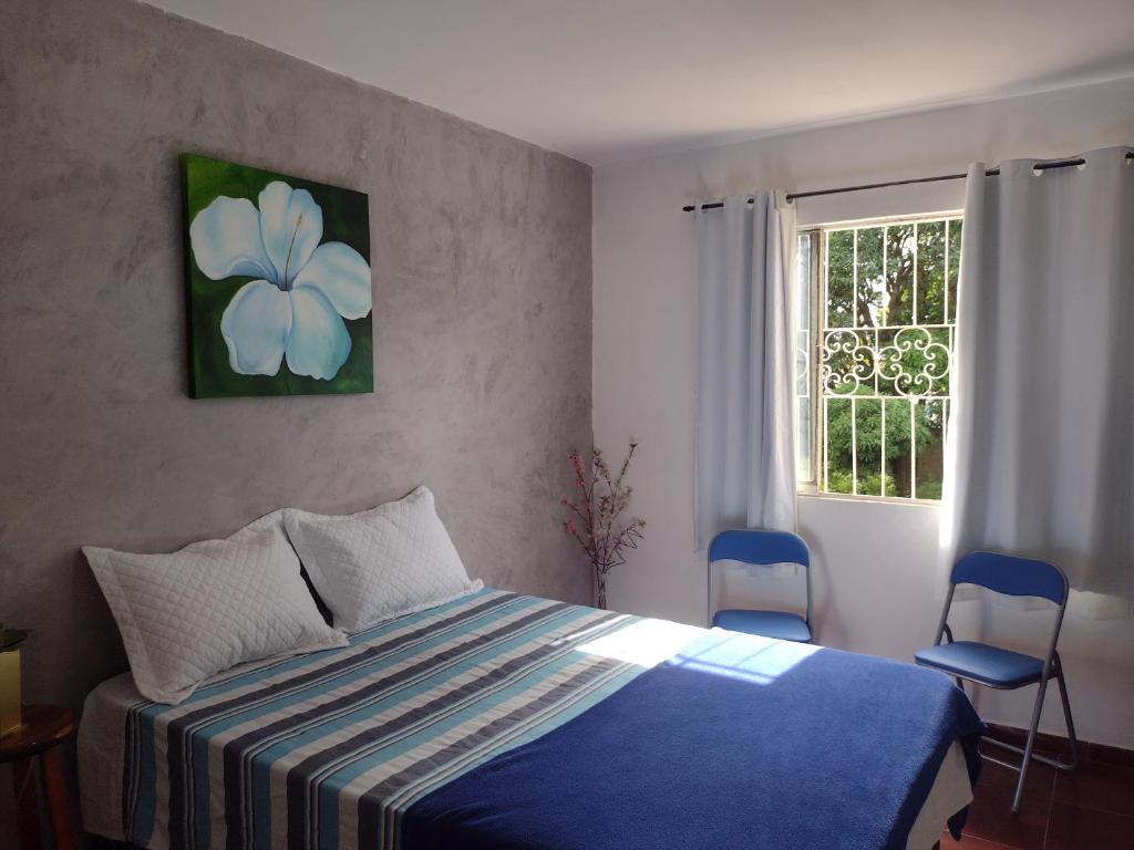 a bedroom with a bed and a window with two chairs at Pousada Jardins in Macaé