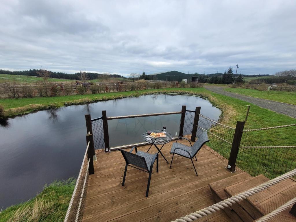 um deque com duas cadeiras e uma mesa ao lado de um lago em The Cabin at Forestview Farm em Greenisland