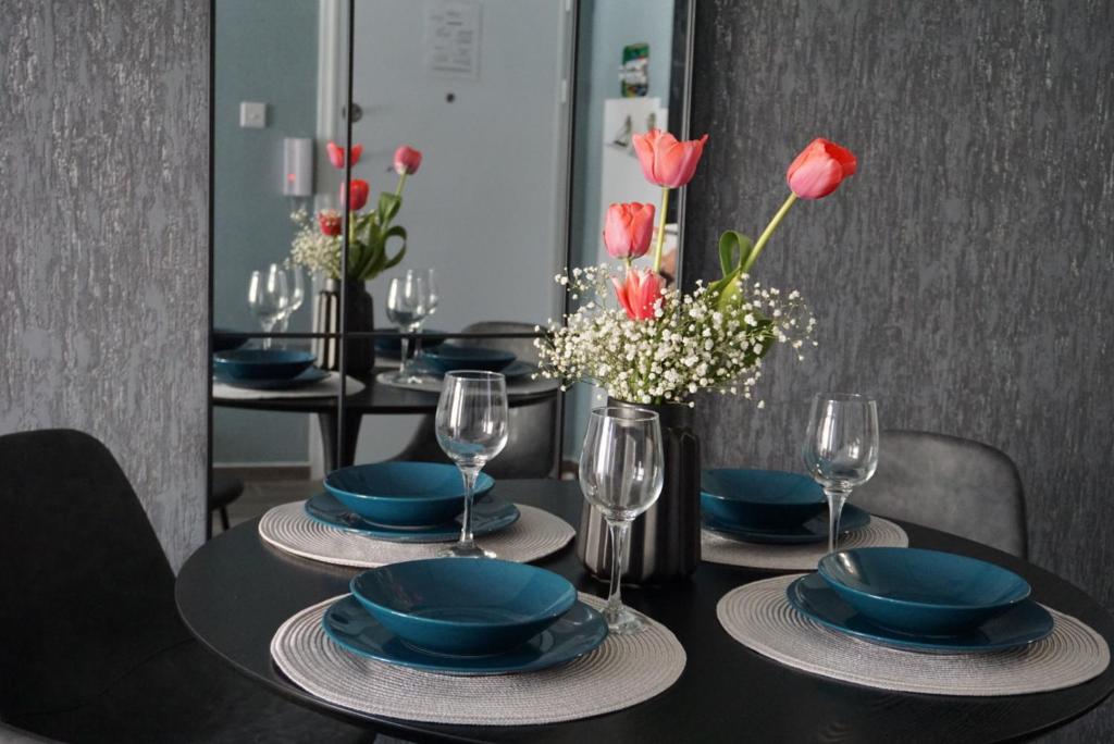 a black table with blue plates and glasses and red flowers at KORZO SUITES PACEVILLE in St. Julianʼs