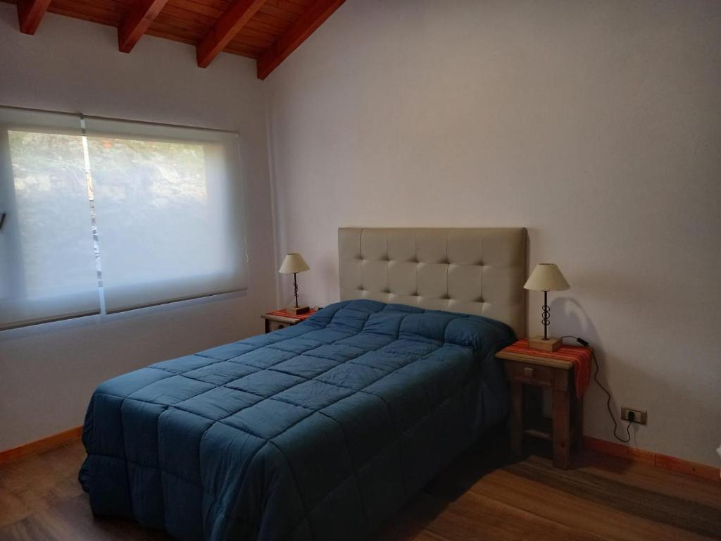 Un dormitorio con una cama azul y una ventana en Sueños de Montaña en Villa Yacanto