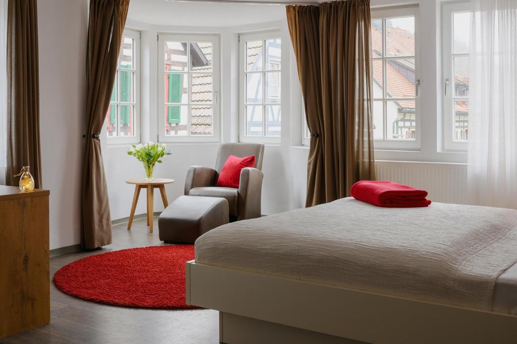 Un dormitorio con una cama y una silla y ventanas. en Adler Schiltach Boutique Hotel und Restaurant, en Schiltach