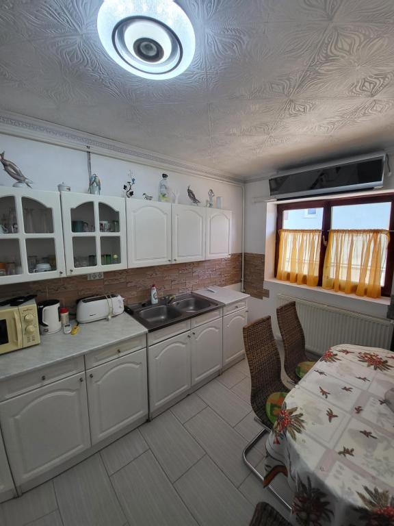 a kitchen with white cabinets and a sink and a table at Almás vendégház in Tiszaújváros