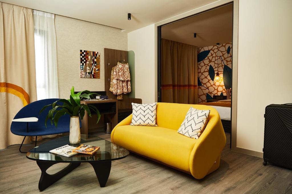 a living room with a yellow couch and a table at ONOMO Hotel Abidjan in Abidjan