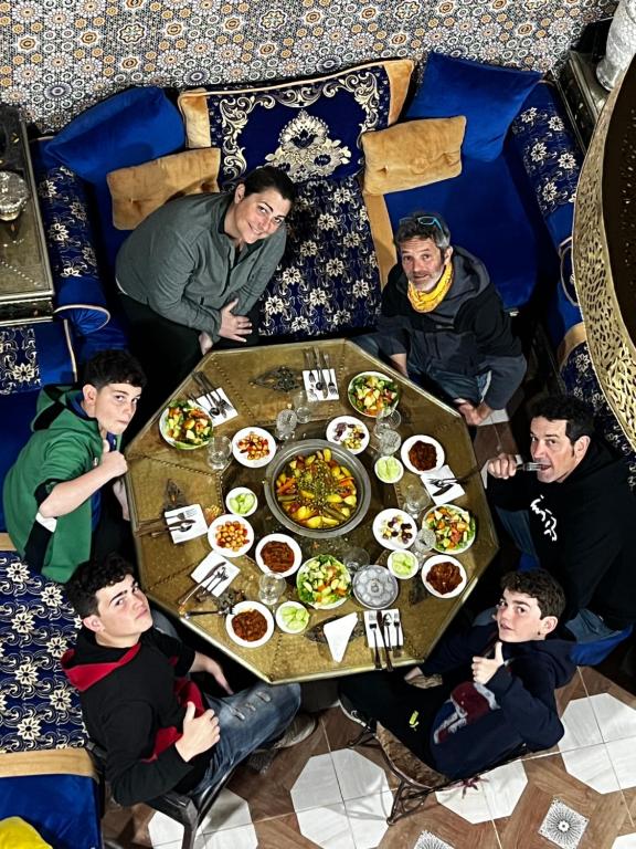 eine Gruppe von Menschen, die an einem Tisch mit Essen sitzen in der Unterkunft Riad Abqari Youssefi in Fès
