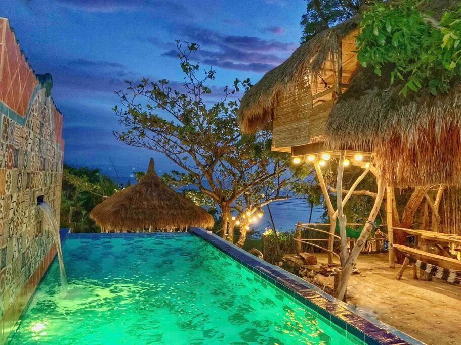 a swimming pool in a resort with a thatch roof at Tree House by the Ocean ( for 2 guests) in Calatagan
