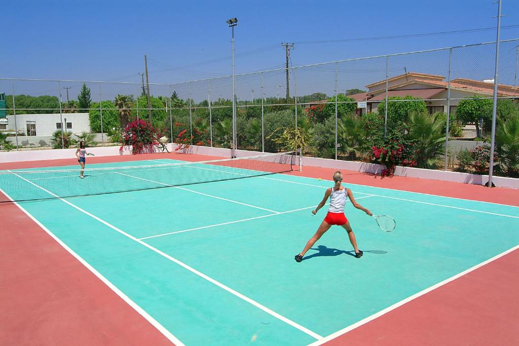 two women playing tennis on a tennis court at Nissiana Hotel & Bungalows in Ayia Napa