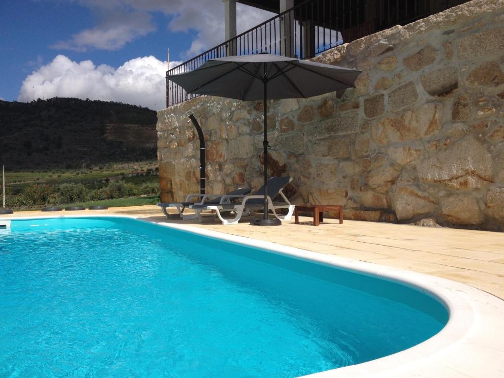 a blue swimming pool with an umbrella and a chair and a table at Quinta do Palame in Vila Flor