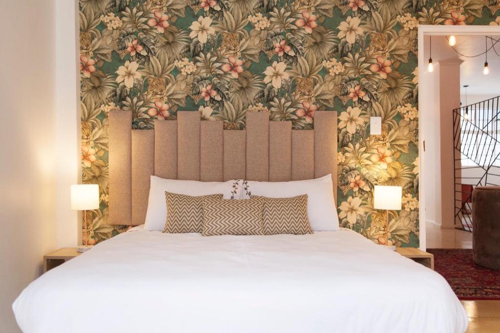 1 dormitorio con 1 cama blanca grande y papel pintado con motivos florales en The City Club, en Ciudad del Cabo