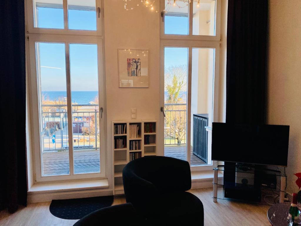 a living room with large windows and a chair and a television at Villa Anna App. 7 Seeblick in Heringsdorf