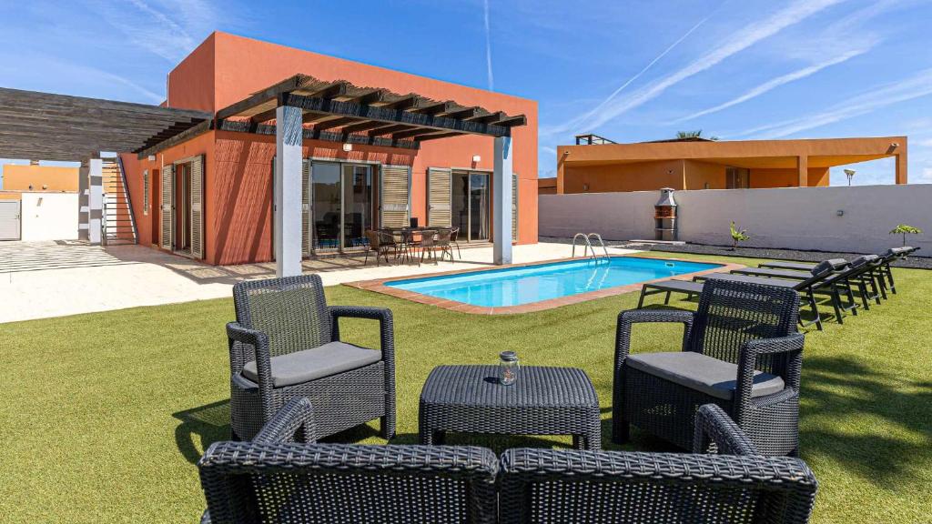 un patio con sillas, una piscina y una casa en Villa Jarcia by Calima Villas, en Caleta de Fuste