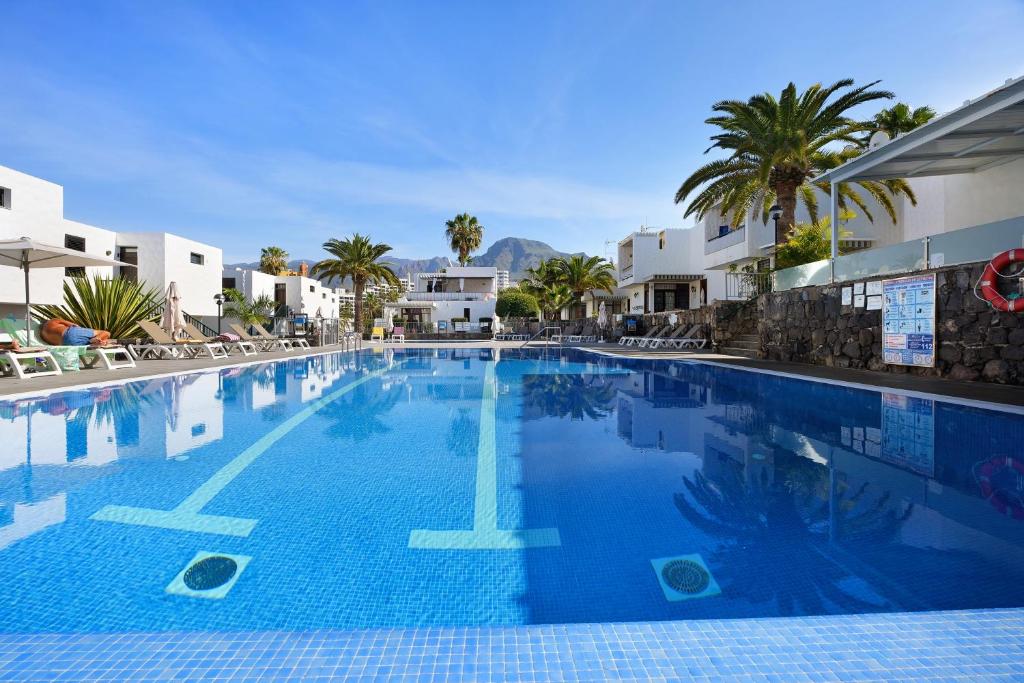 a large swimming pool with palm trees and buildings at Bungamerica272 in Playa de las Americas