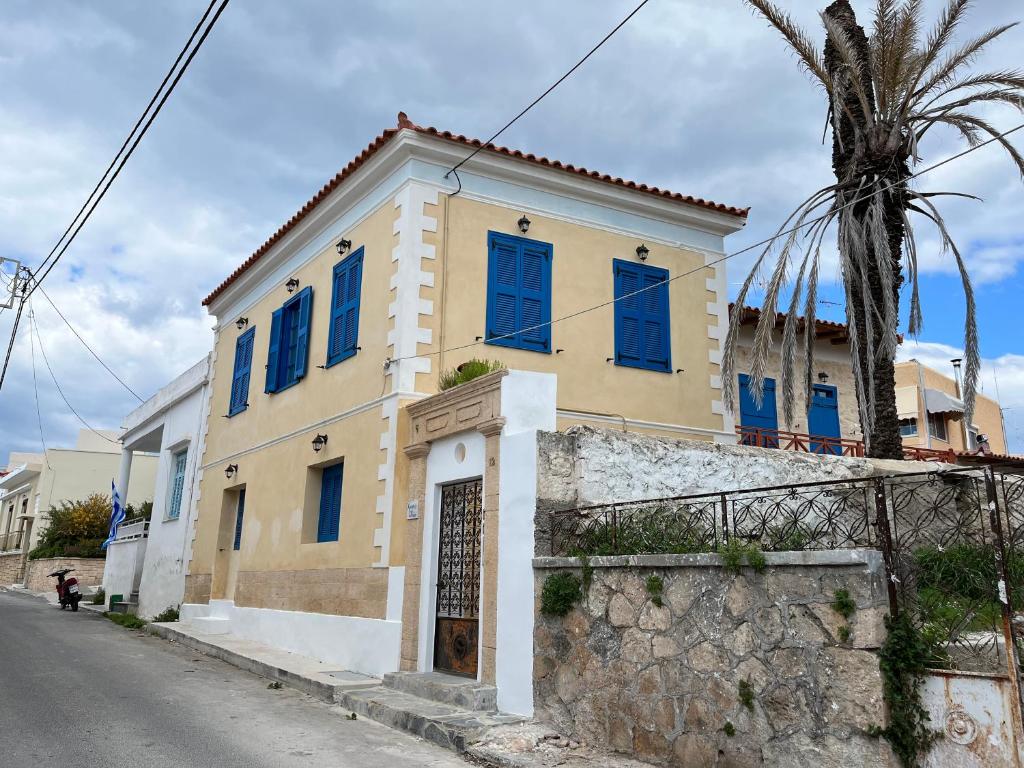 uma casa amarela com janelas azuis numa rua em Chrysiis 2 em Egina