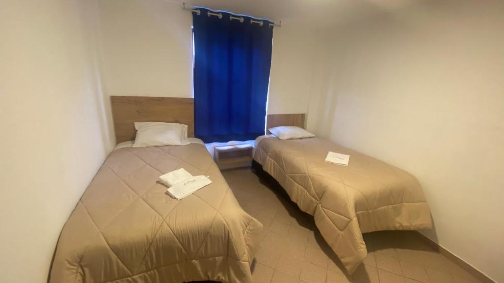 a room with two beds and a window with blue curtains at La Pascana Hospedaje in Cajamarca