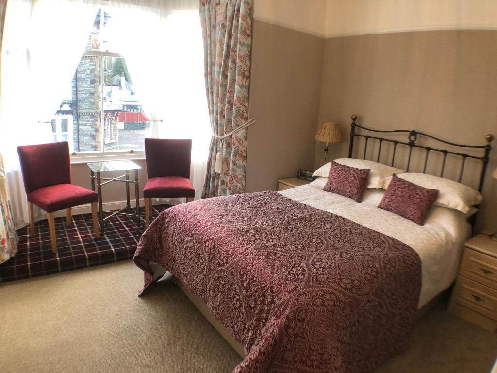 a bedroom with a bed and two chairs and a window at Tarn Hows in Keswick