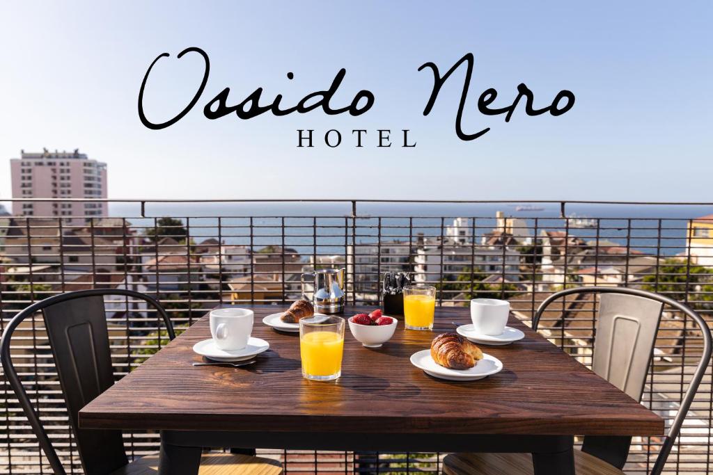 een houten tafel met eten en drinken op een balkon bij Hotel Ossido Nero in Viña del Mar