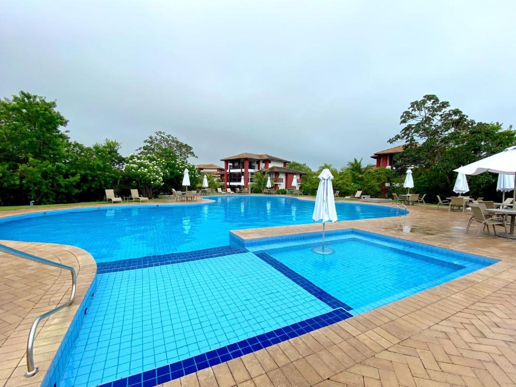 a large blue swimming pool with a white umbrella at VILLAGE DAS ACÁCIAS NO PISCINAS NATURAIS in Mata de Sao Joao