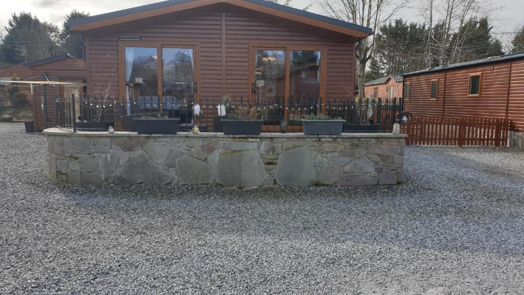 une cabane en rondins avec un mur en pierre en face d'une maison dans l'établissement Red Squirrel Lodge, à Auchterarder