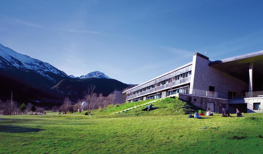 un edificio con gente sentada en el césped delante de él en MónNatura Pirineus - AJOOO385, en Esterri d'Àneu