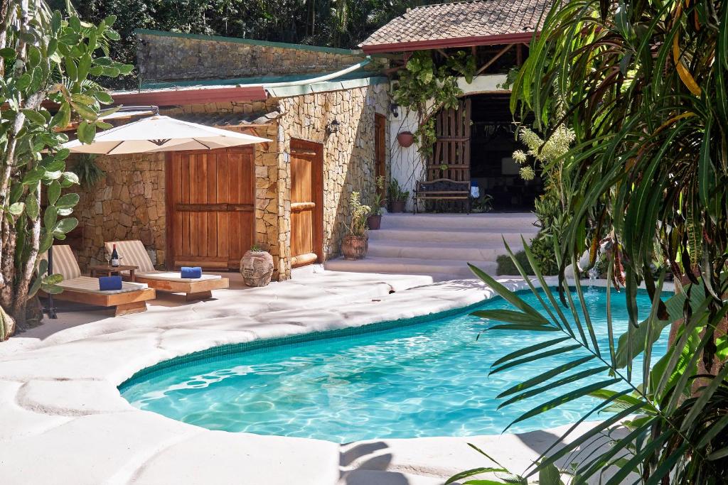 a swimming pool next to a house with an umbrella at Villa Havana in Mal País