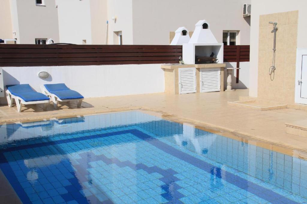 una gran piscina con 2 sillas azules al lado en Maricosta Villas, en Protaras