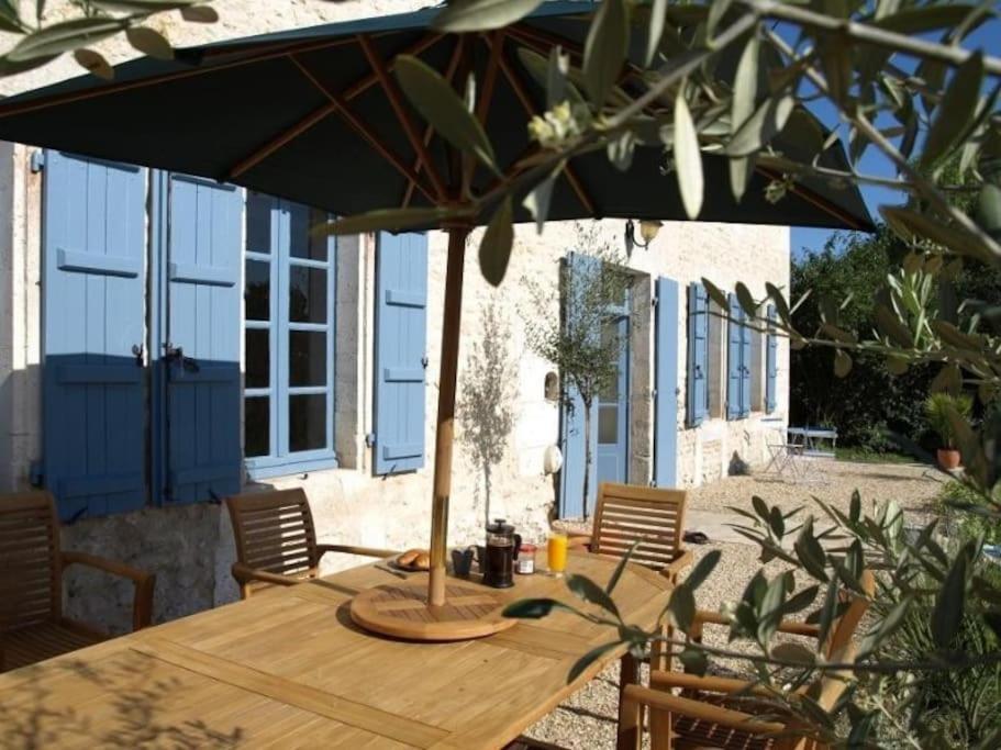 einen Holztisch mit Sonnenschirm auf einer Terrasse in der Unterkunft Beautiful renovated farmhouse with pool & gardens in Nonac
