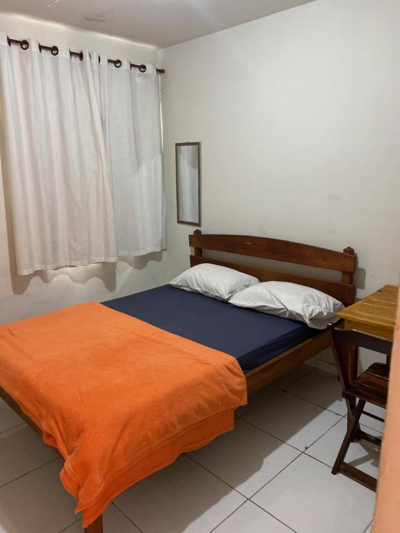 a bedroom with a bed with an orange blanket and a desk at Pousada Serra Carioca Friburgo in Nova Friburgo