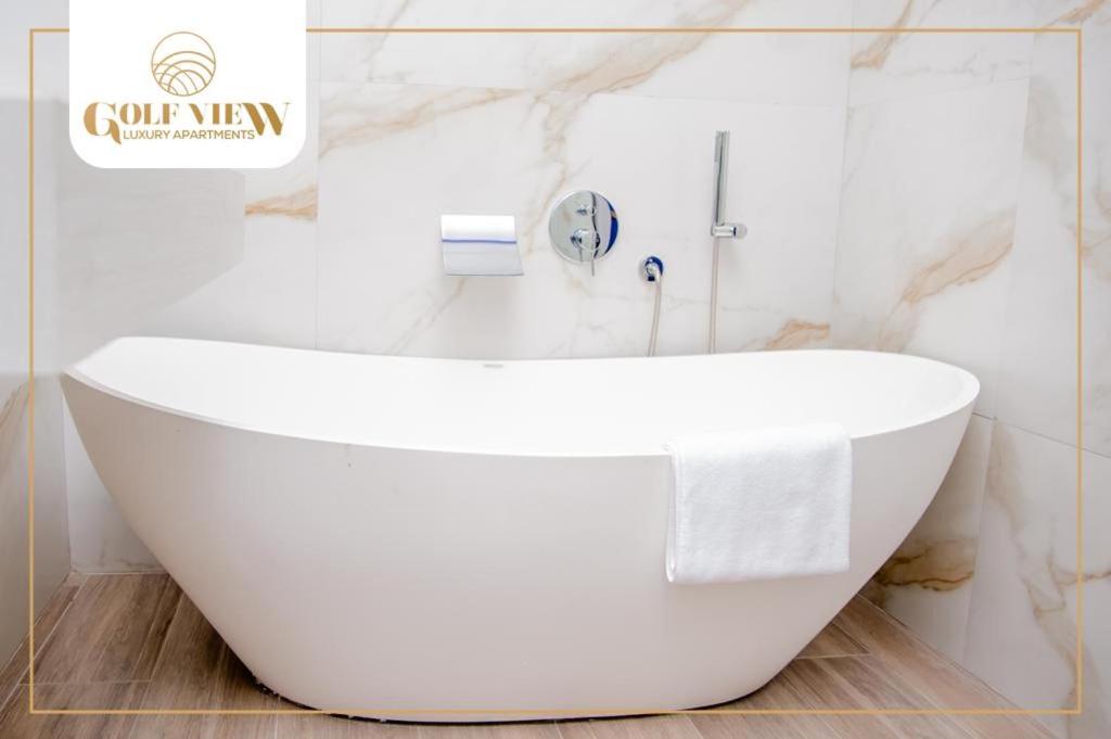 y baño con bañera blanca y paredes de mármol. en Golfview luxury apartment, en Richards Bay