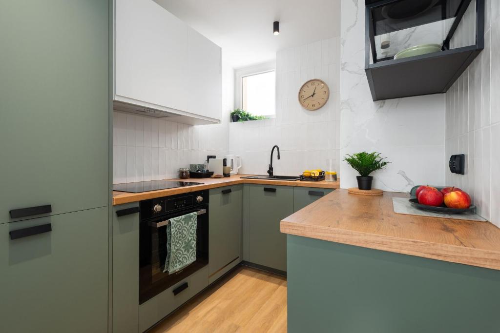 a kitchen with green cabinets and a clock on the wall at Apartament Amber - darmowy Parking, ścisłe centrum - by Kairos Apartments in Gliwice