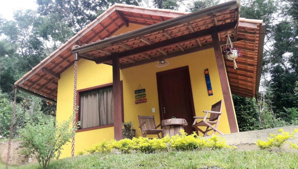 a small yellow house with a porch and two chairs at POUSADA CHALÉS DA GROTA de SÃO PEDRO DA SERRA- NOVA FRIBURGO in Nova Friburgo