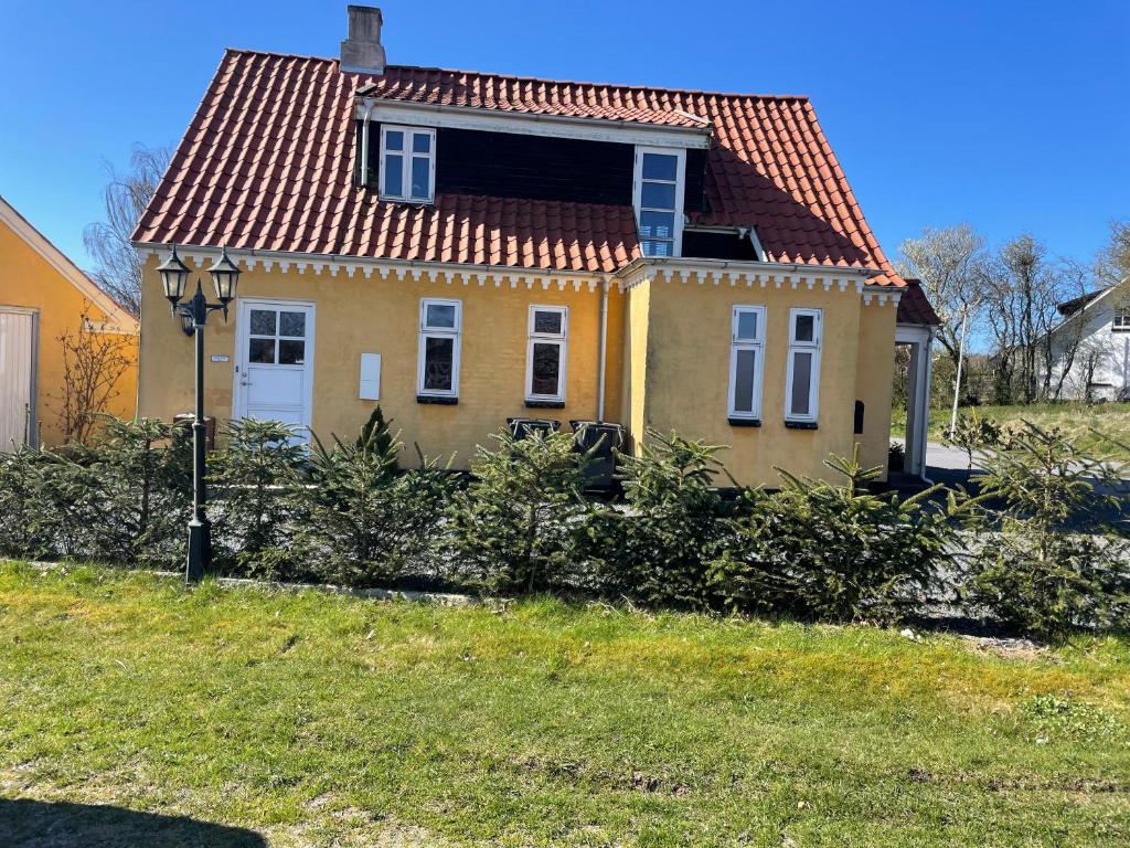 una pequeña casa amarilla con techo rojo en Bjergly, en Hjørring