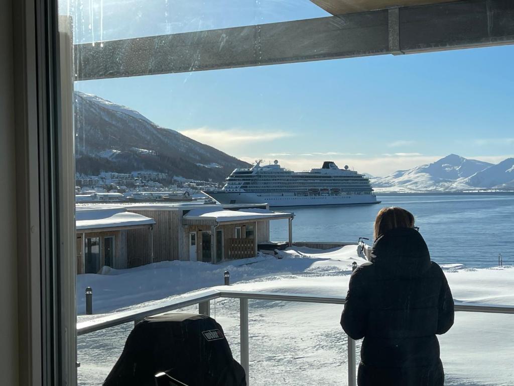 Una mujer mirando por la ventana en un crucero en Ocean view apartment, en Tromsø