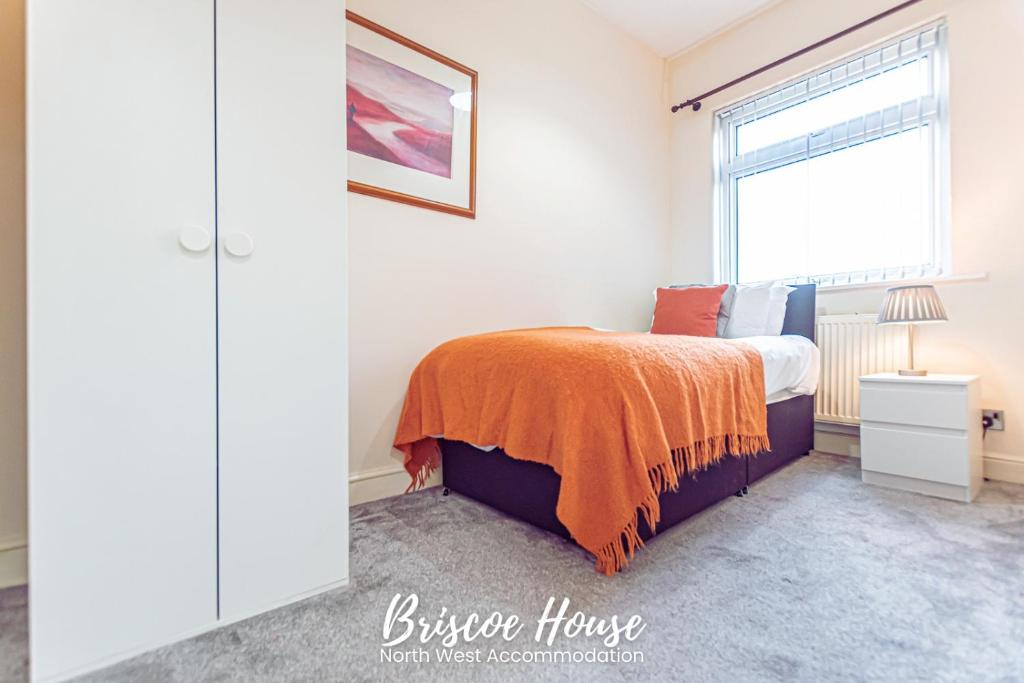 a bedroom with a bed with an orange blanket on it at Briscoe Serviced Accommodation in Manchester