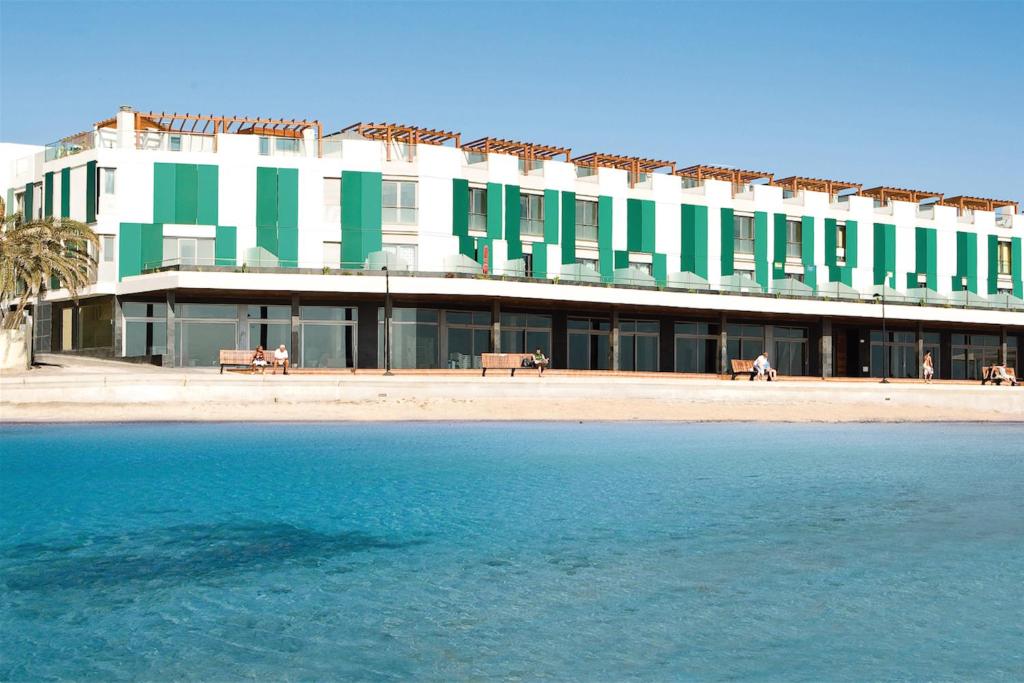 a large building with green and white windows next to the water at Hotel LIVVO Corralejo Beach in Corralejo