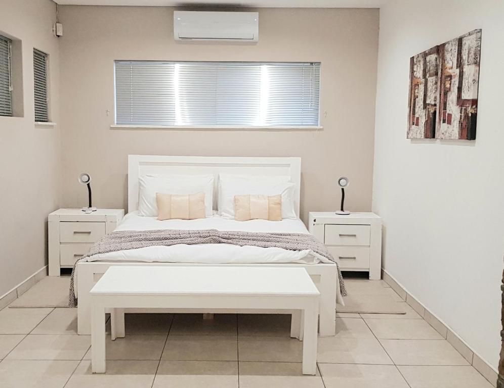 a white bedroom with a white bed and two night stands at Feather Self Catering Accommodation in Windhoek