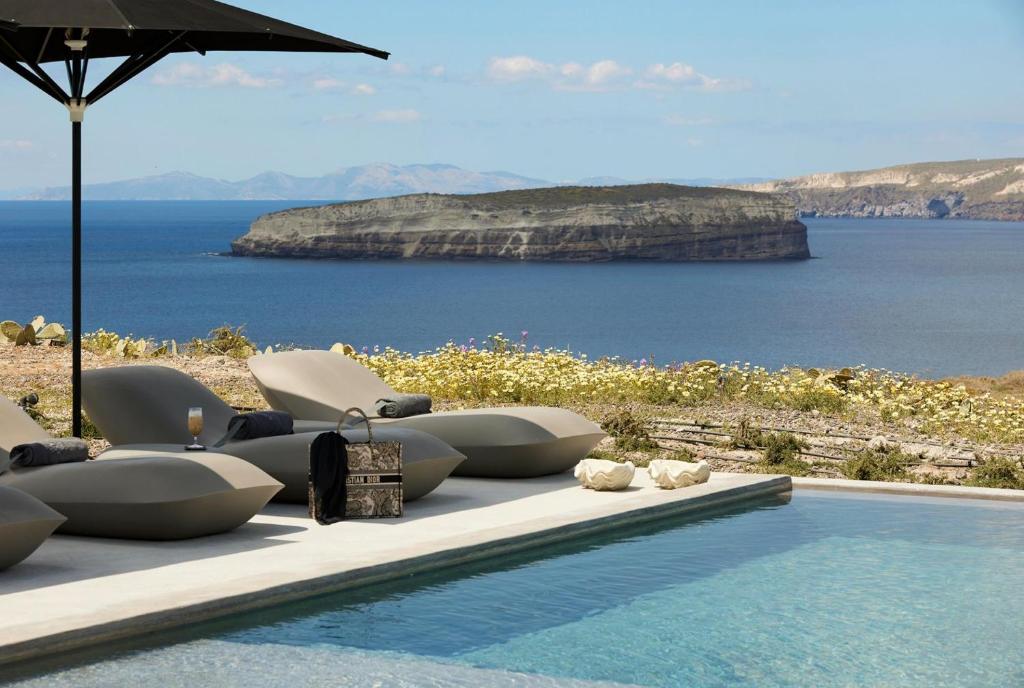 ein Pool mit Stühlen und ein Regenschirm neben dem Wasser in der Unterkunft Absolute Paradise Santorini in Akrotiri