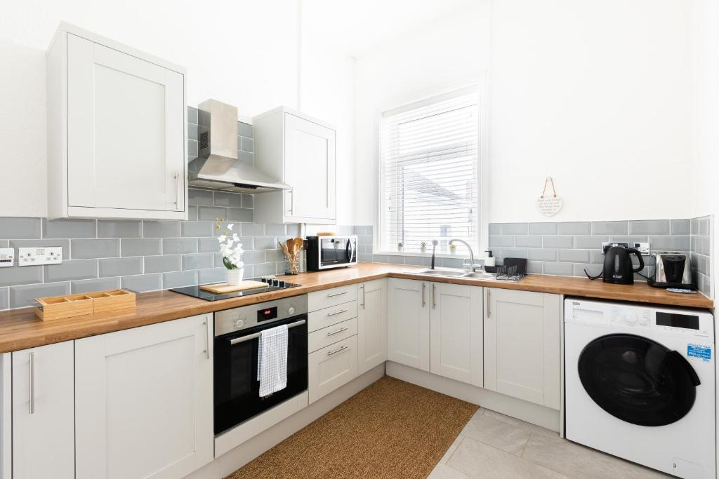 a white kitchen with white cabinets and a sink at Judah Suites by Koya Homes - TV Bed Apartment, Central High Street, Free Parking in Barry