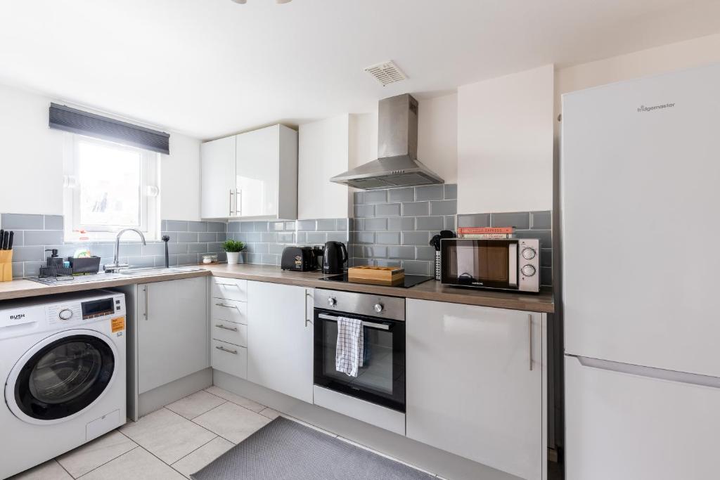 a kitchen with white cabinets and a washer and dryer at Judah Suites by Koya Homes - TV Bed Apartment, Central High Street, Free Parking in Barry