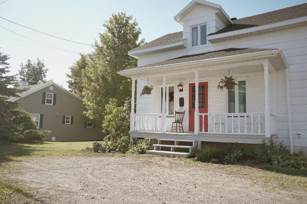 Casa blanca con puerta roja y silla en el porche en La petite maison du voisin en Mont-Carmel