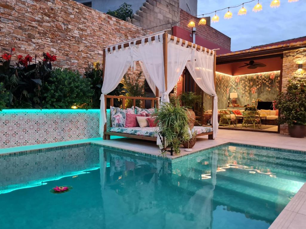 una pérgola sobre una piscina con una cama al lado de una casa en El Jardin de Gala, en Castejón de Monegros