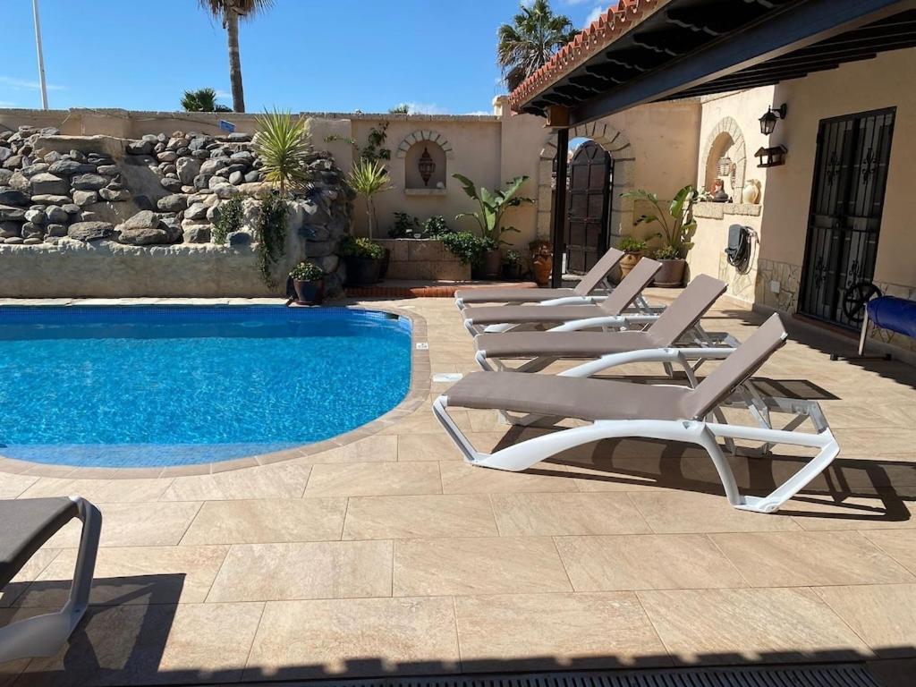 a row of lounge chairs next to a swimming pool at Casa Paraiso Villa Tenerife, stunning family bungalow with totally secluded pool area, wheelchair friendly in San Miguel de Abona