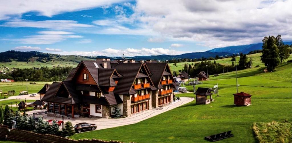 una casa grande en un campo verde con montañas en Hotel Zawrat - KROK NA STOK!, en Białka Tatrzanska