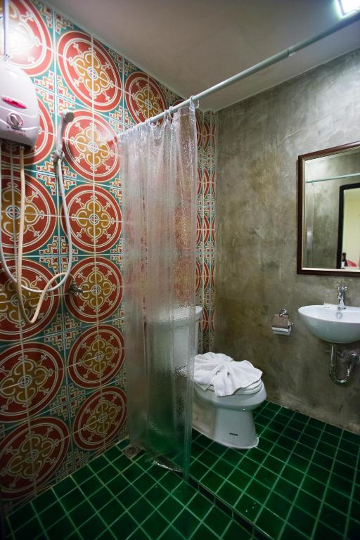 A compact bathroom has a patterned tile shower, toilet, and wall-mounted basin.