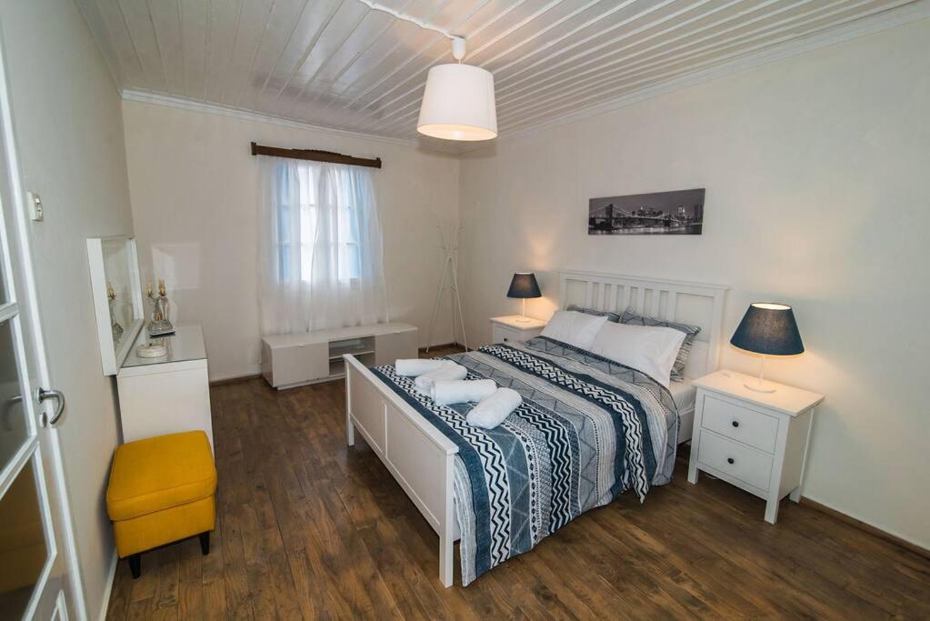 een witte slaapkamer met een bed en een gele stoel bij Avli Townhouse in Skopelos Town
