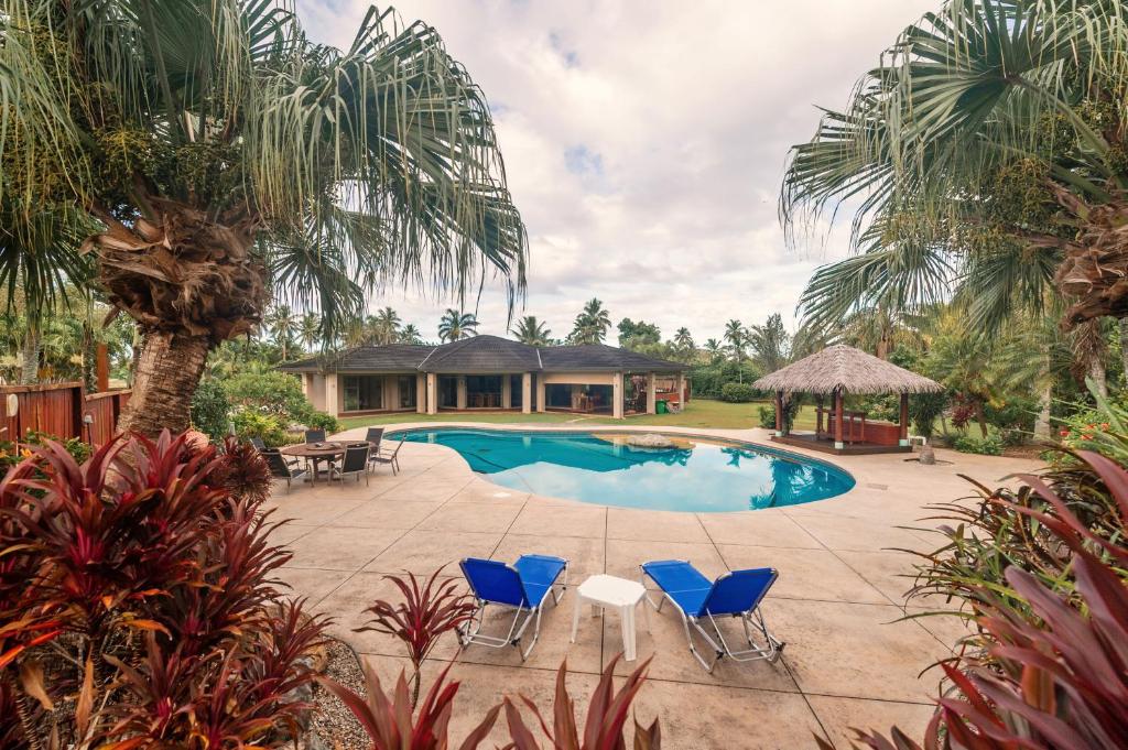 a swimming pool with blue chairs and a house at GT - Rarotonga Fishing Lodge in Rarotonga