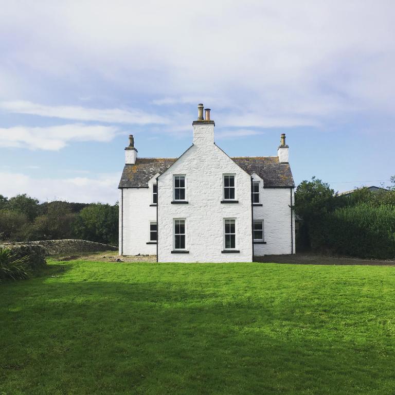 an old white house with a large grass field at Longhill Farmhouse in Whithorn