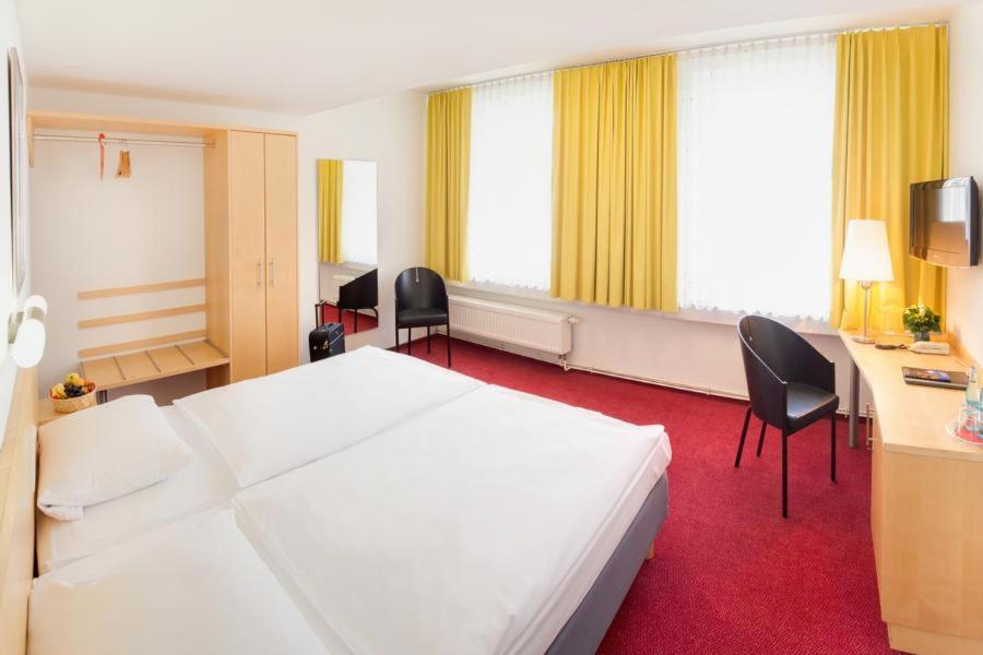 a hotel room with a white bed and a desk and chairs at CVJM Düsseldorf Hotel & Tagung in Düsseldorf