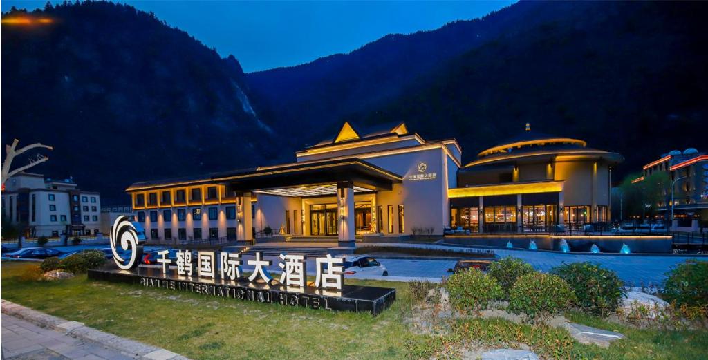 a large building in front of a mountain at night at Qianhe International Hotel in Jiuzhaigou