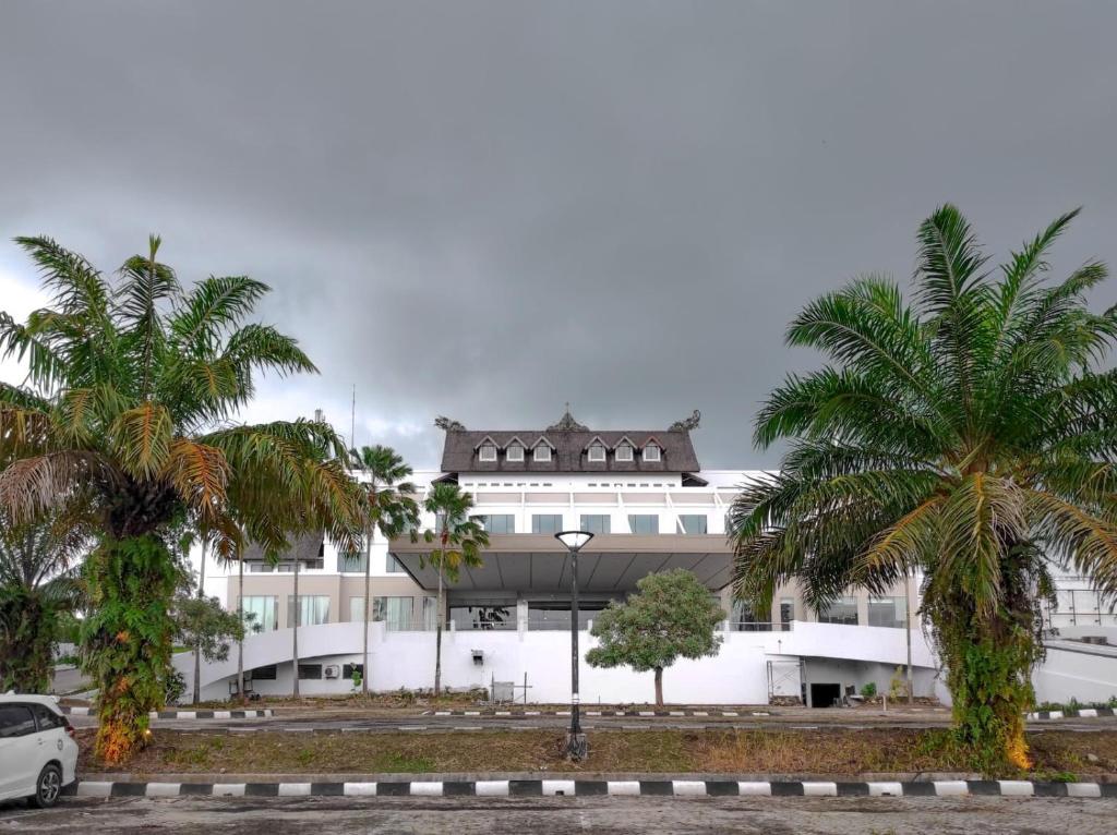 un bâtiment blanc avec des palmiers devant lui dans l'établissement Horison Ultima Bandara Balikpapan, à Sepinggang-Kecil