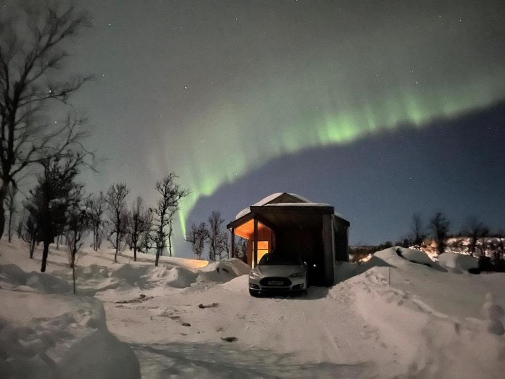a cabin with a car in the snow under the aurora at Skarvhytta - moderne hytte med flott beliggenhet in Seim
