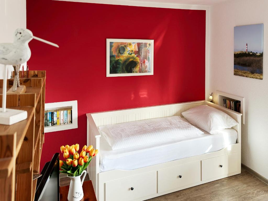 ein Schlafzimmer mit einer roten Wand und einem weißen Bett in der Unterkunft Haus Diana *Ferienwohnung Wattenmeer* in Wittdün